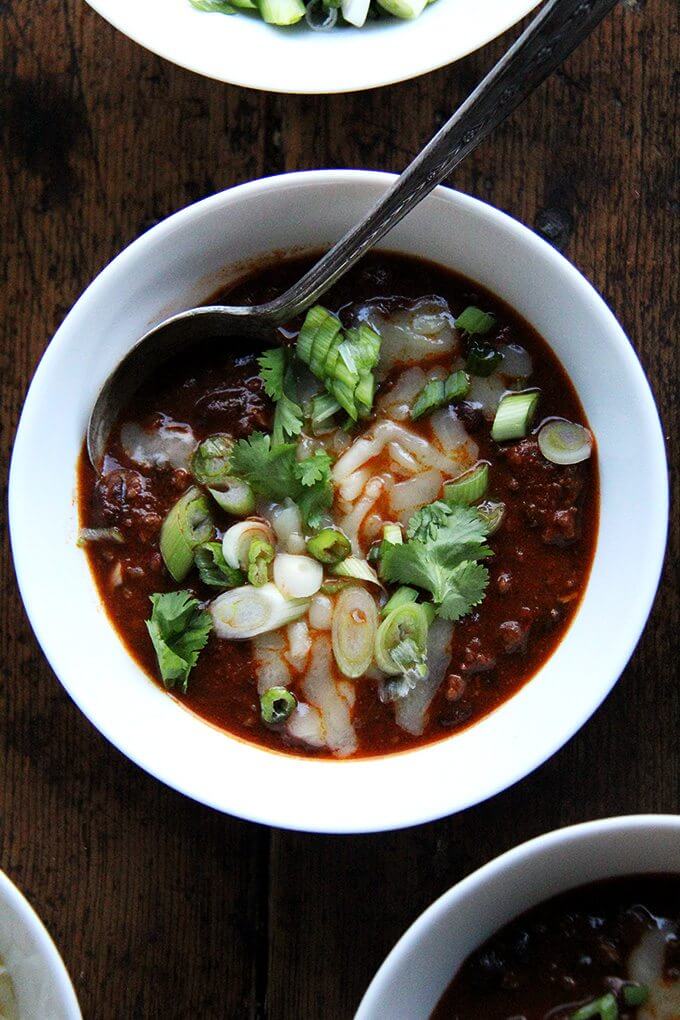 A bowl of weeknight chili topped with cheddar, scallions and cilantro.
