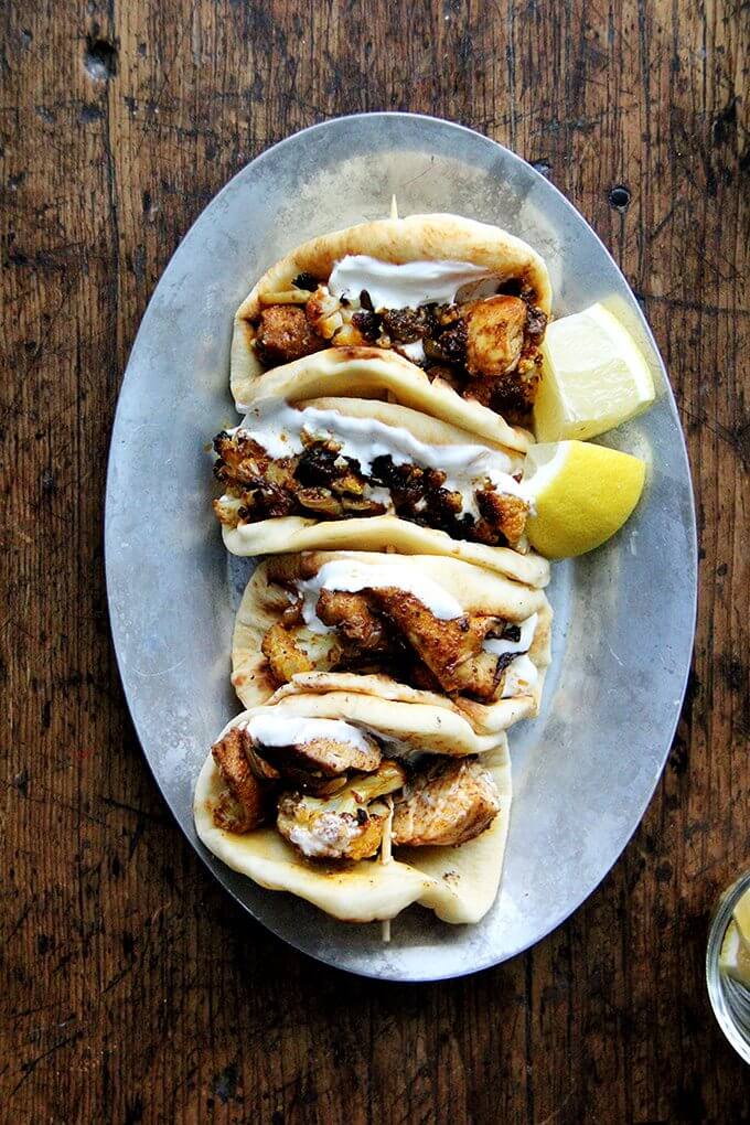 A sizzle platter of chicken and cauliflower shawarma in mini pita on a platter. 