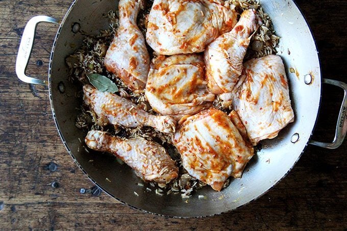 An overhead shot of a sauté pan with onion, ras-el-hanout, rice, and chicken.