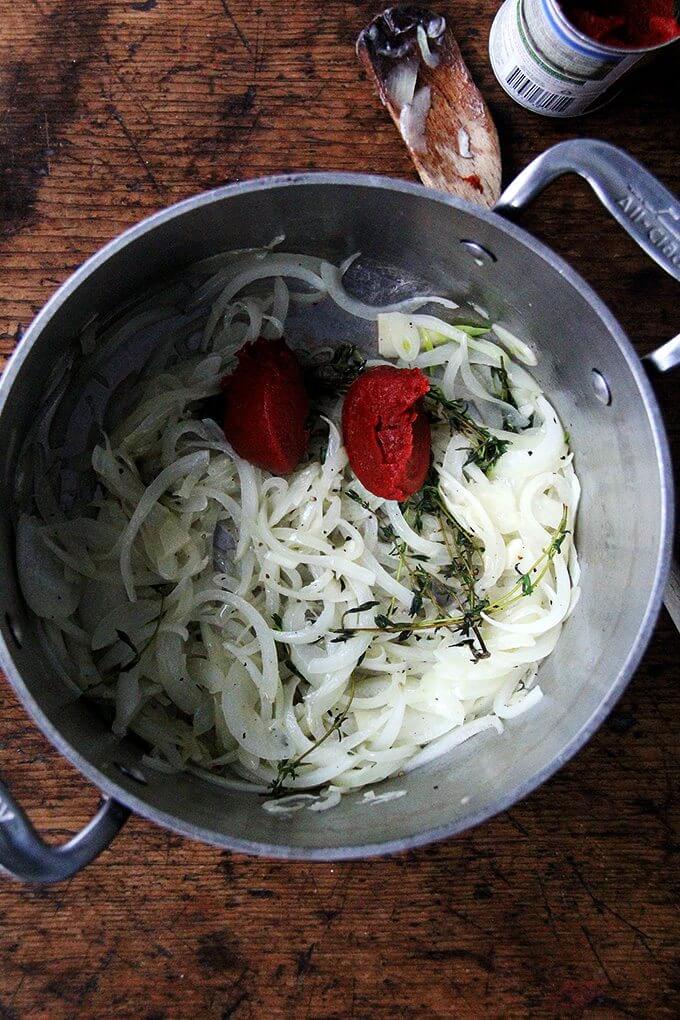 A large pot filled with sautéed onions, garlic, and thyme with the addition of tomato paste.