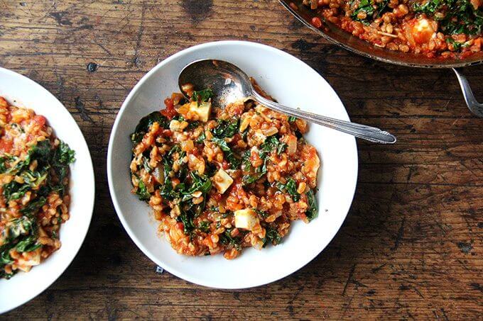 A bowl of farro risotto with kale and feta with a spoon. 