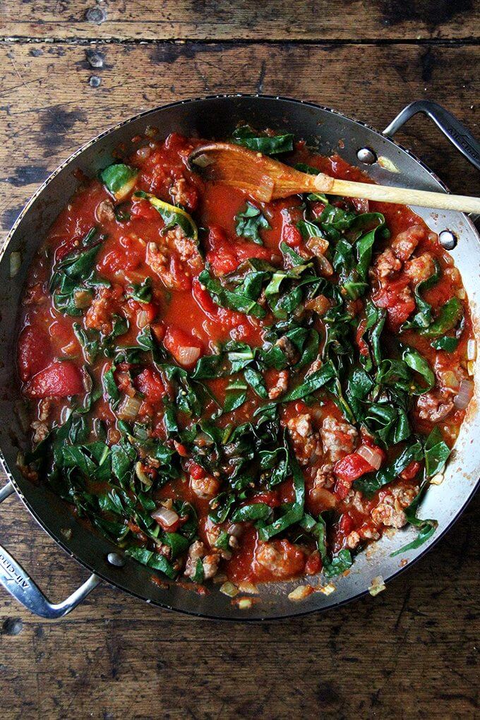 A sauté pan filled with a pan of tomato sauce made with sausage and Swiss chard.