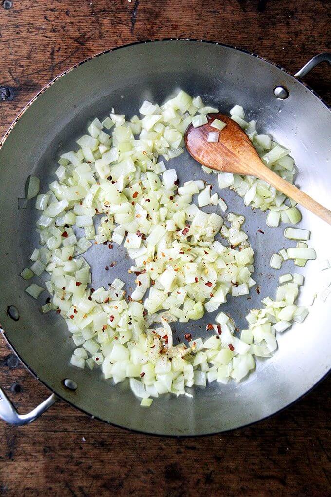 A sauté pan with onions and crushed red pepper flakes.