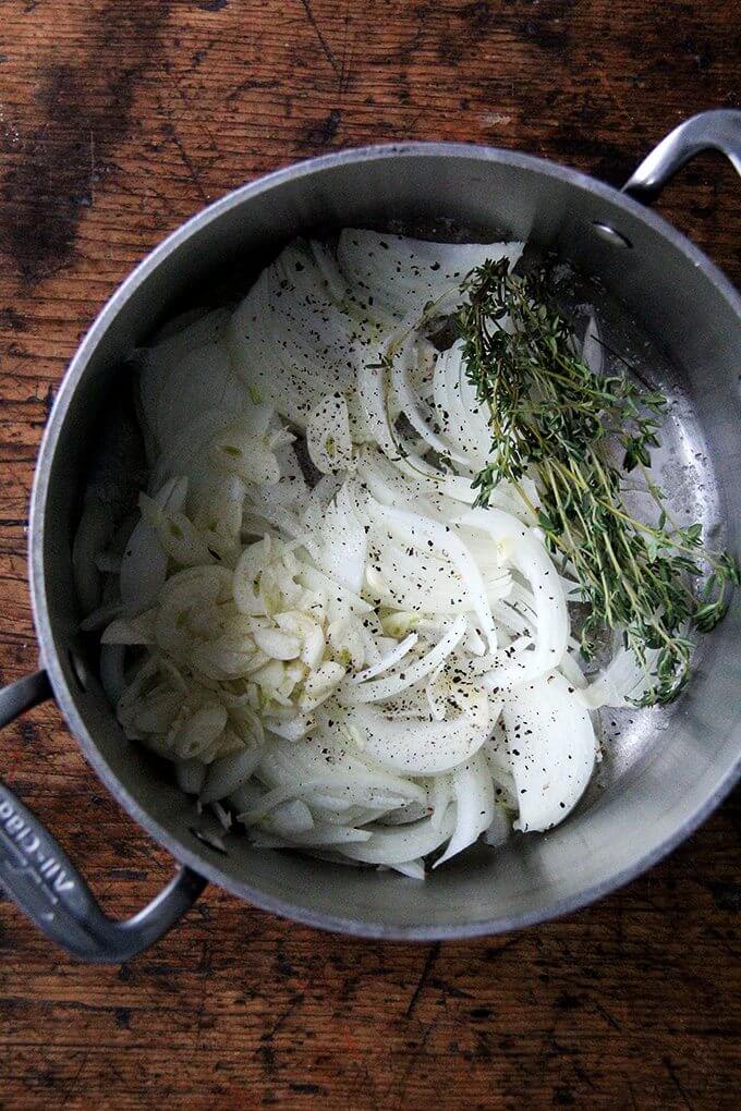 A large pot filled with onions, garlic, salt, pepper, and thyme.