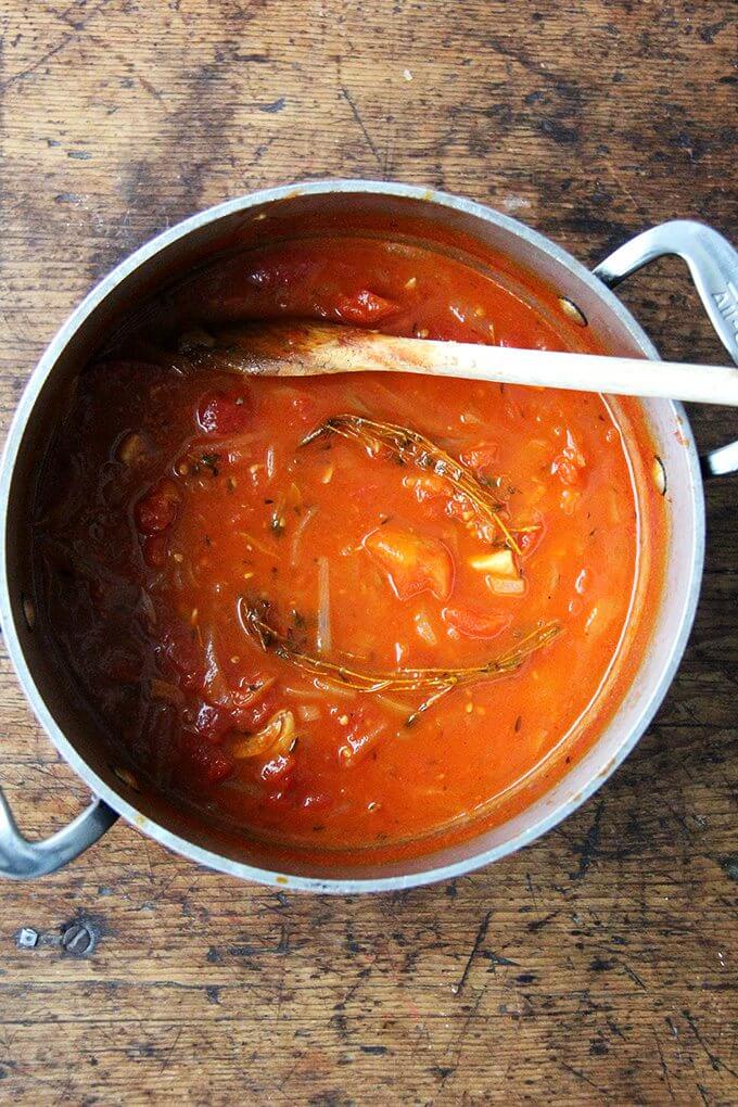 A large pot of cooked pantry tomato soup with a spoon in it.