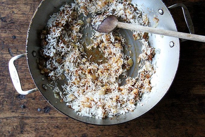 An overhead shot of a sauté pan with onion, ras-el-hanout, and rice.