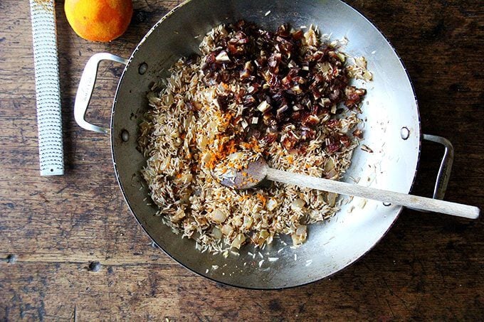 An overhead shot of a sauté pan with onion, ras-el-hanout, rice, dates, and orange zest.