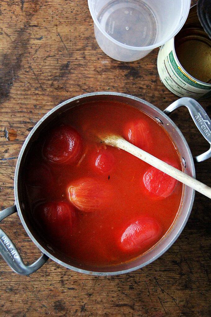 A large pot filled with cooked onions, garlic, tomato paste and a can of plum tomatoes. 