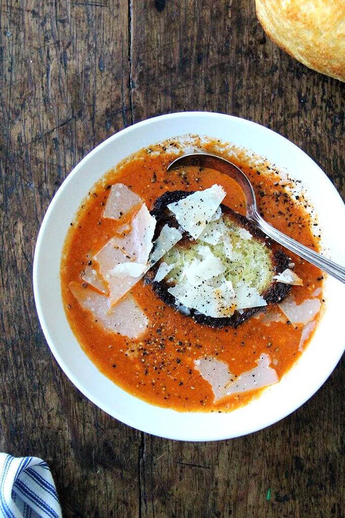 An overhead shot of a bowl of pantry tomato soup with a hunk of bread and shavings of parmesan.