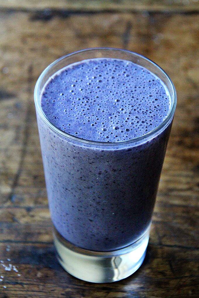 A tall glass filled with a blueberry-almond smoothie.