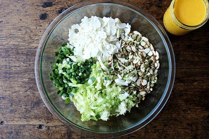 A bowl with all of the ingredients for the cabbage salad: cabbage, scallions, cauliflower, almonds, and pepitas.