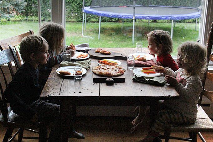 Sideview of 4 kids eating skillet pizza and carrots. 