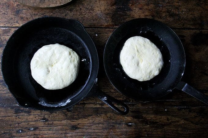 Two cast iron skillets holding pizza dough. 