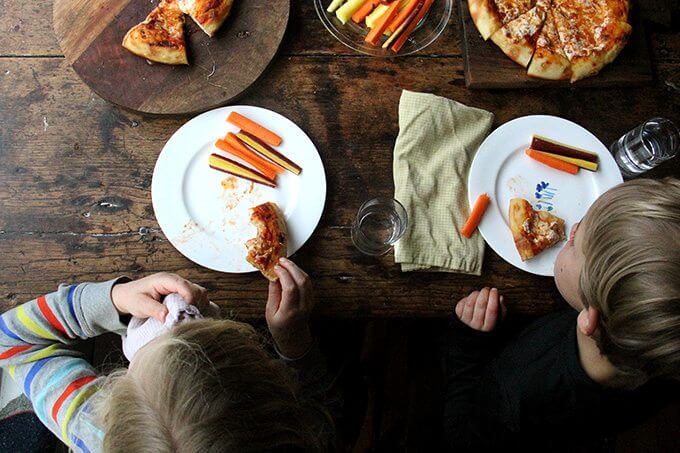 Overhead shot of kids eating skillet pizza and carrots. 