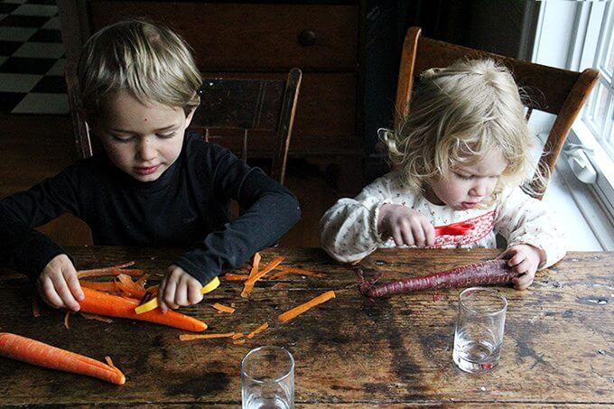 Two kids peel carrots. 