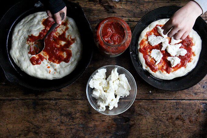 Two kids top two cast iron skillet pizzas.