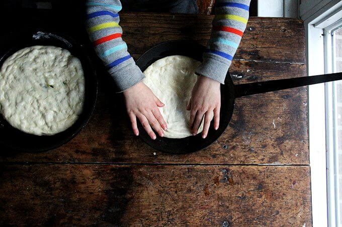 A child spreads pizza dough in a skillet. 