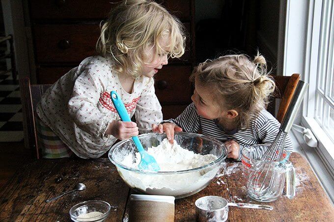 Sideview of two kids making pizza dough. 