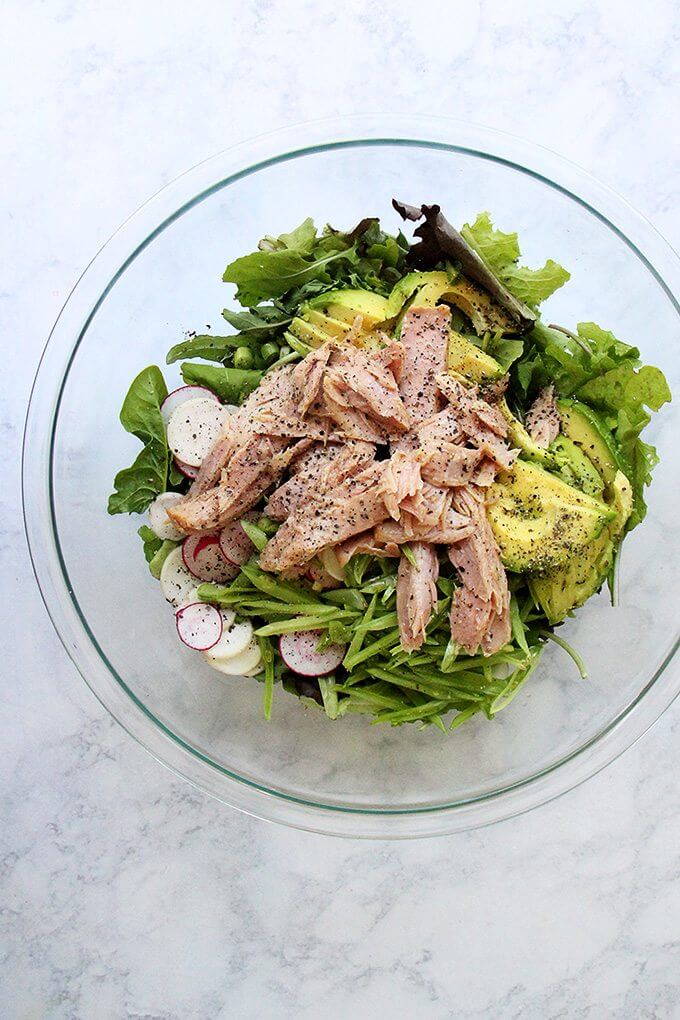 A large bowl filled with a salad of greens, radishes, avocado, jarred tuna and a shallot vinaigrette.