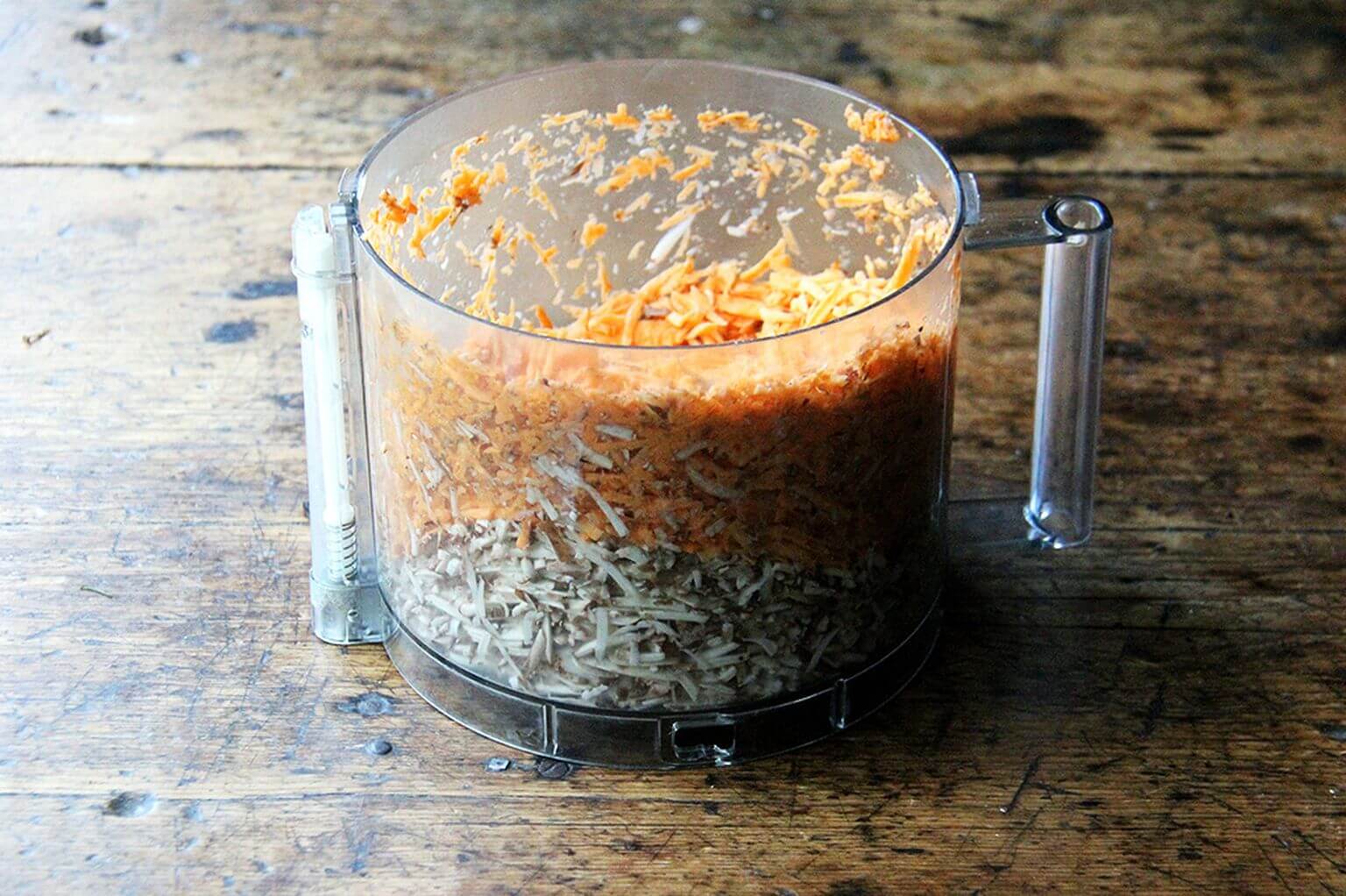 A food processor filled with grated mushrooms and carrots.