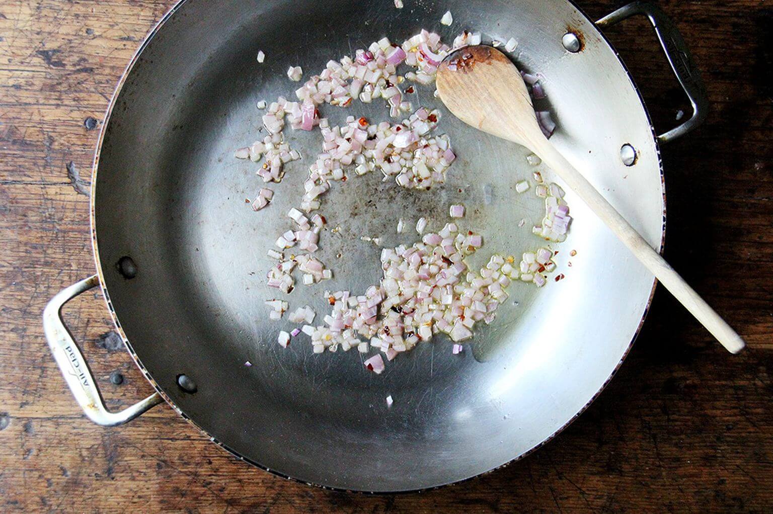 A skillet with an onion sautéing in oil.