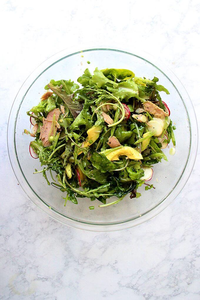 A large bowl filled with a salad of greens, radishes, avocado, jarred tuna and a shallot vinaigrette all tossed together.