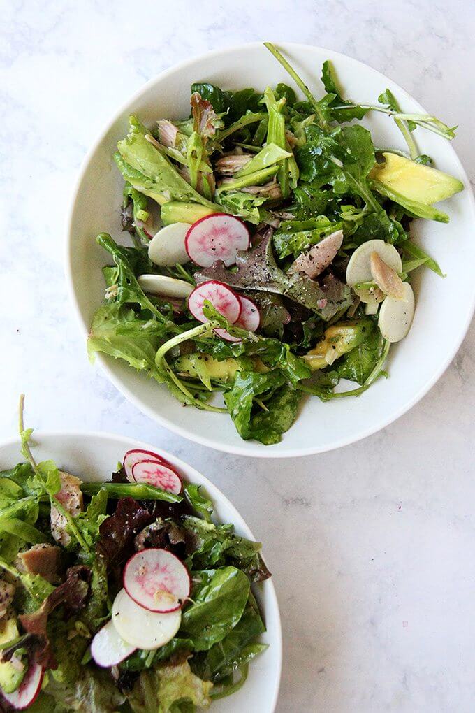 Two bowls filled with a salad of greens, radishes, avocado, jarred tuna and a shallot vinaigrette.