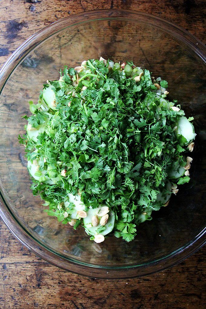 A large bowl filled with salad ingredients: cucumbers, cilantro, peanuts, lime, vinegar, and mint.