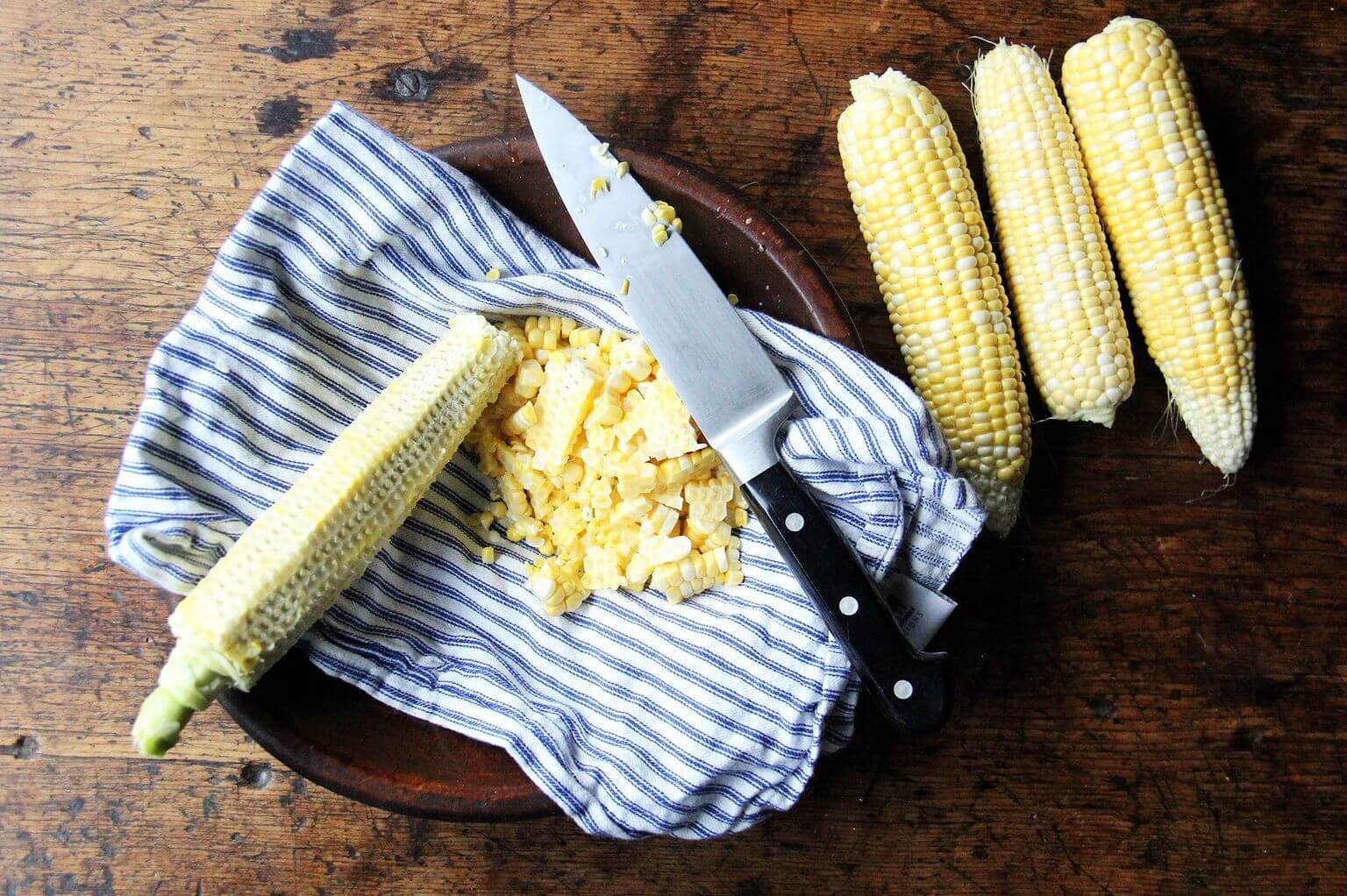 A bowl lined with a towel filled with stripped corn kernels.