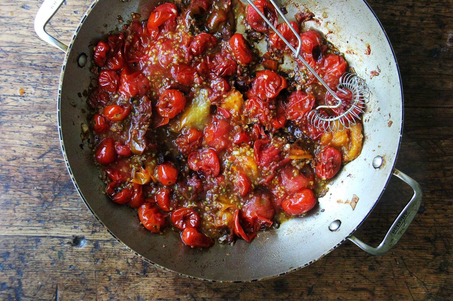 A large skillet with mashed cherry tomatoes.