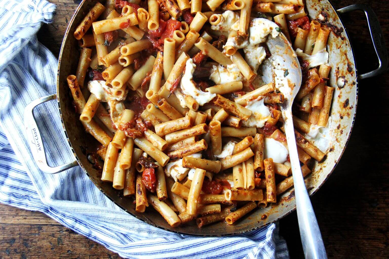 A large skillet of one-pan baked ziti with a spoon.