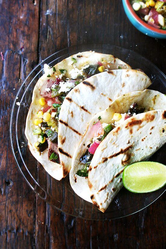 A plate of two steak tacos dressed with grilled corn and poblano salsa.