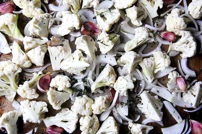 A sheet pan of cauliflower, onions, garlic, and thyme, ready for the oven.