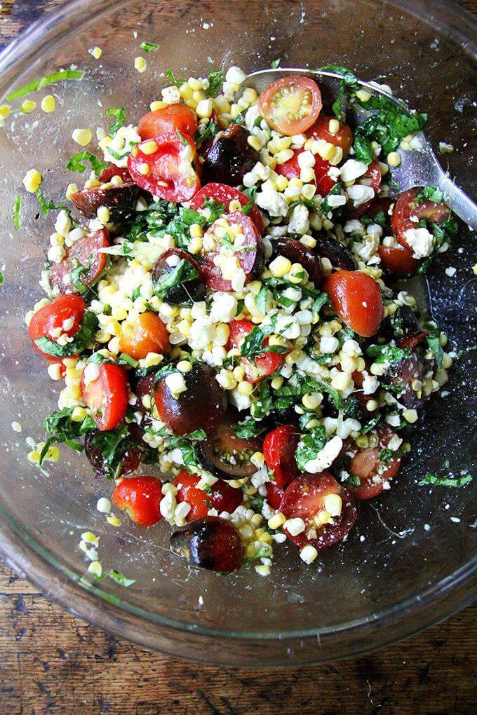 A bowl of raw corn salad with tomatoes and feta.