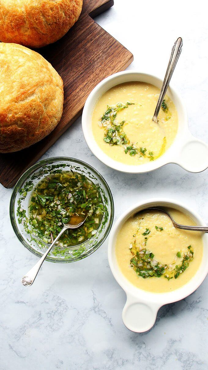 Two bowls of corn soup with herb salsa and bread on the side. 