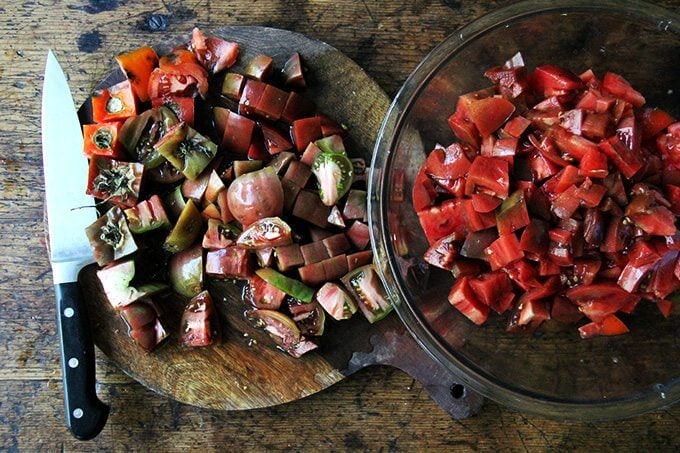 A board of chopped tomatoes aside a bowl of chopped tomatoes.