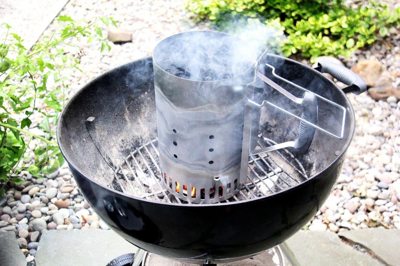 A charcoal grill holding a chimney starter with burning coals.