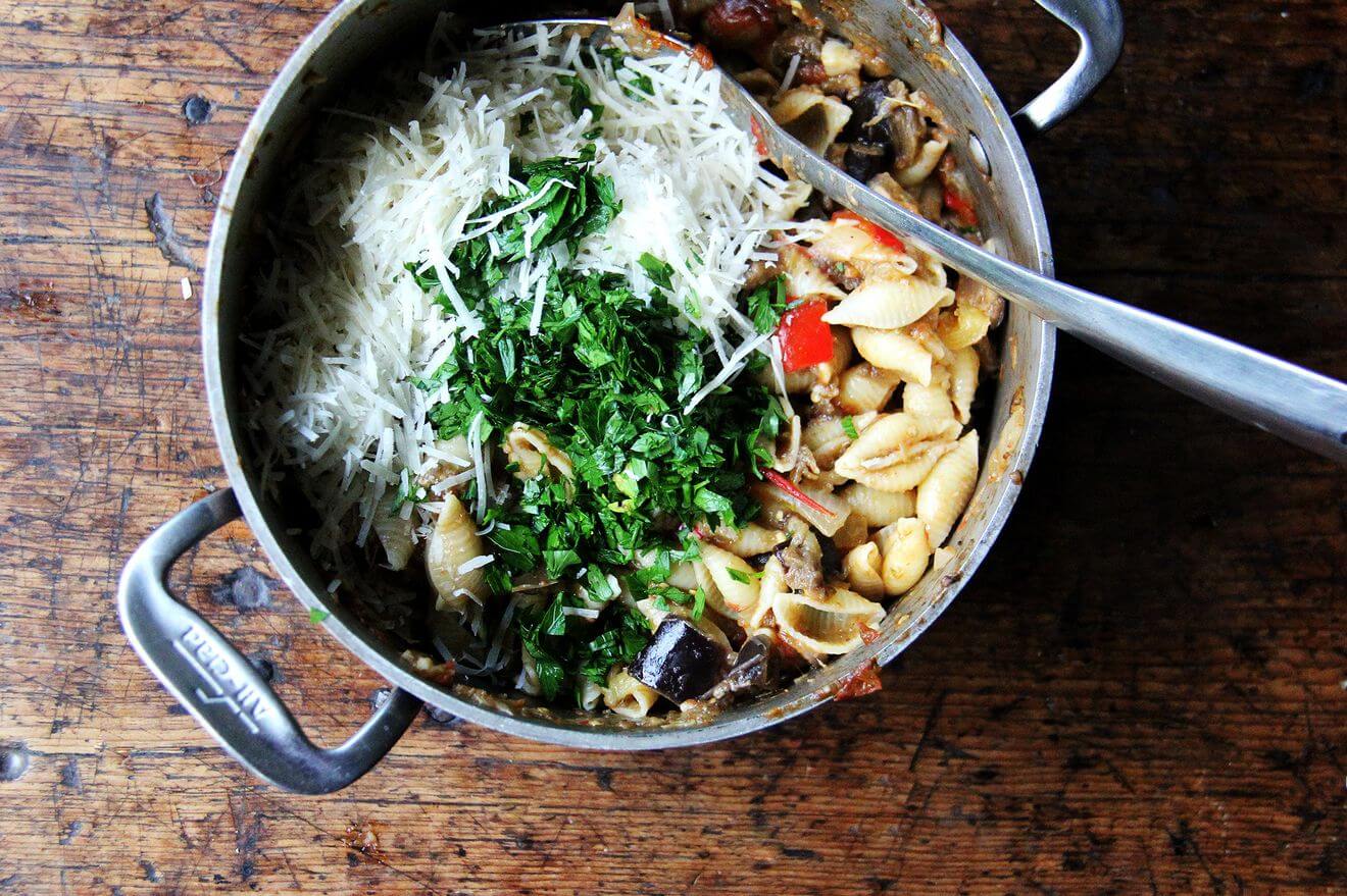 A medium pot with pasta, roasted ratatouille, parmesan and basil.