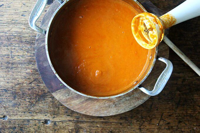 A pot of puréed tomato sauce aside an immersion blender.