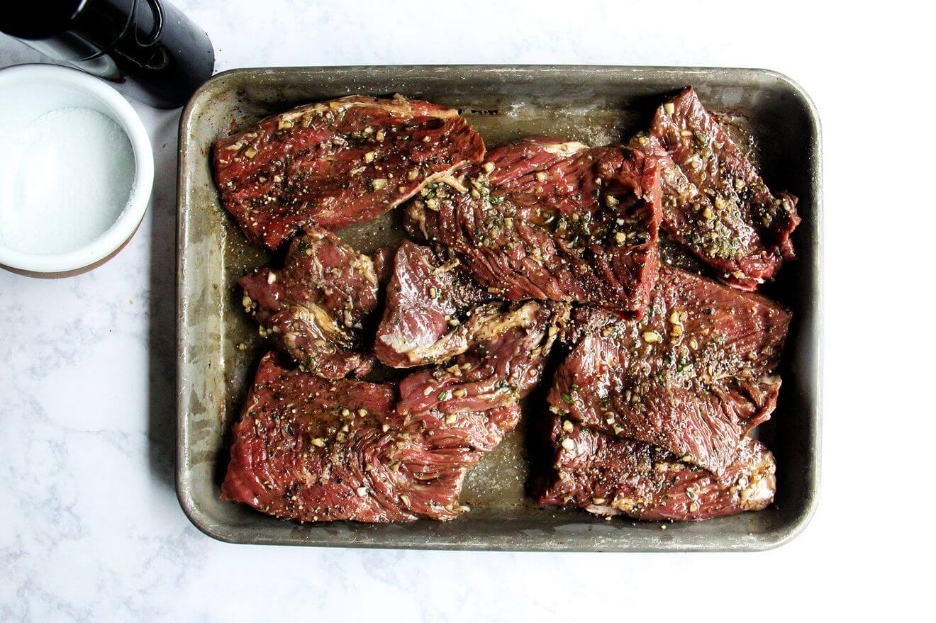 A sheet pan holding marinating hanger steaks, salt, and pepper. 