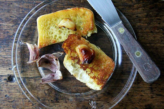 A plate topped with bread and whole cloves of roasted garlic. 