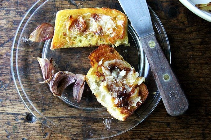 A plate topped with bread and whole cloves of roasted garlic spread across the bread. 