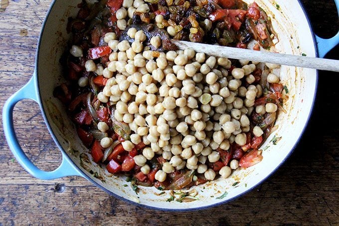 A Le Creuset braiser filled with sautéed tomatoes and chickpeas.