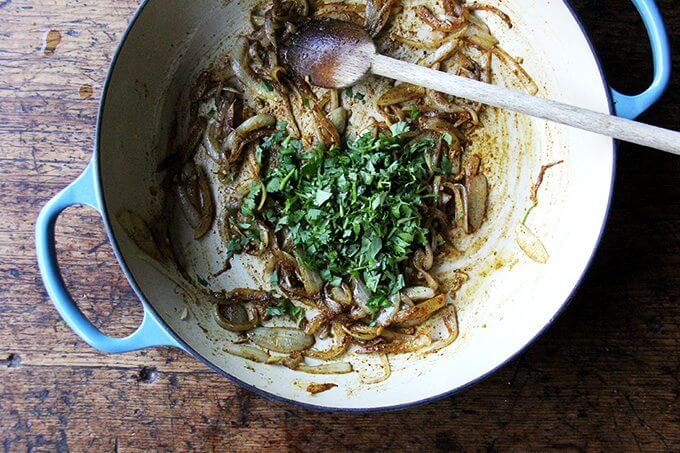 A Le Creuset braiser filled with sautéed onions and cilantro.