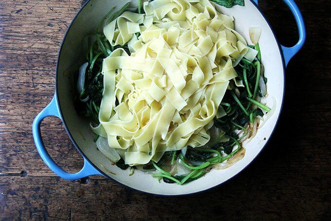 An overhead shot of a skillet filled with sautéed greens and cooked pasta. 