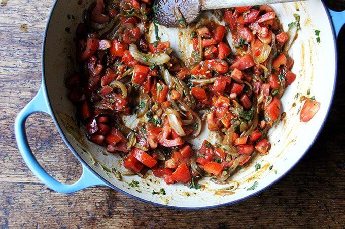 A Le Creuset braiser filled with sautéed onions and tomatoes.