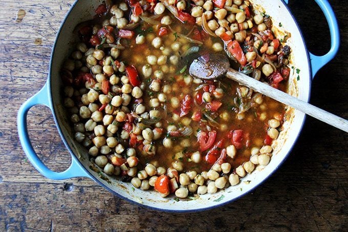 A Le Creuset braiser filled with chickpea tagine, tomatoes, and water.