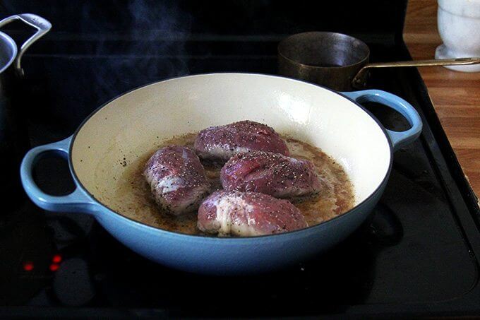 Four duck breasts cooking in a large Le Creuset braiser, stovetop. 