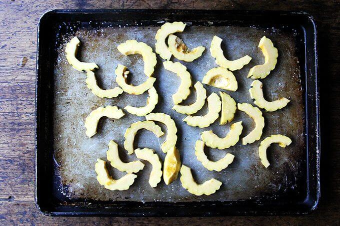 Sliced, raw delicata squash on a sheet pan.