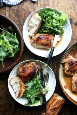Overhead shot of two dinner plates filled with one-pot chicken with sherry and sherry vinegar sauce, bread, and salad.